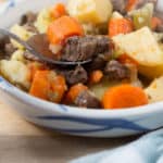 a spoon filled with instant pot beef stew in a shallow bowl